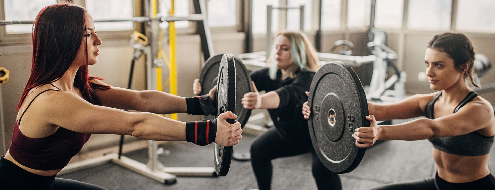 Women focused during a strength training workout with weight plates at Gold’s Gym East End in Richmond VA, representing real results and fitness passion